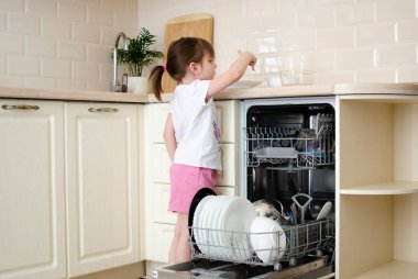 Mutfakta bulaşık makinesinden tabakları çıkarmaya yardım eden tatlı bir kız. Annenin küçük yardımcısı. Mutfak.
