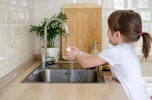 Girl washes hands in the kitchen with soap.