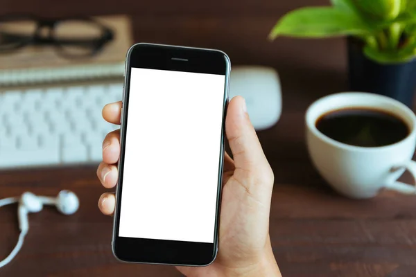 Primer plano mano sosteniendo la pantalla blanca del teléfono sobre la mesa de trabajo —  Fotos de Stock