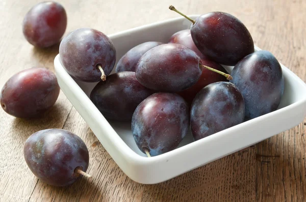 Prunes violettes dans un bol blanc sur fond de table en bois — Photo