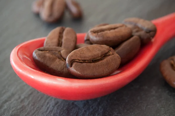 Grains de café dans une cuillère rouge sur fond de tableau — Photo