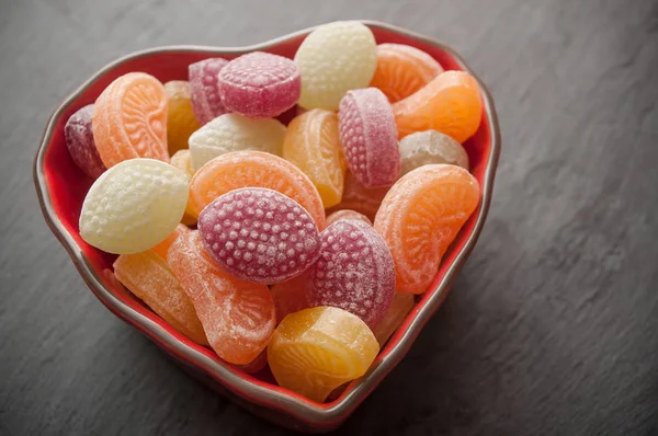Caramelos tradicionales en un cuenco con forma de corazón sobre fondo de pizarra — Foto de Stock