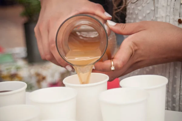 Manos de mujer vertiendo jugo de manzana en vasos de plástico —  Fotos de Stock