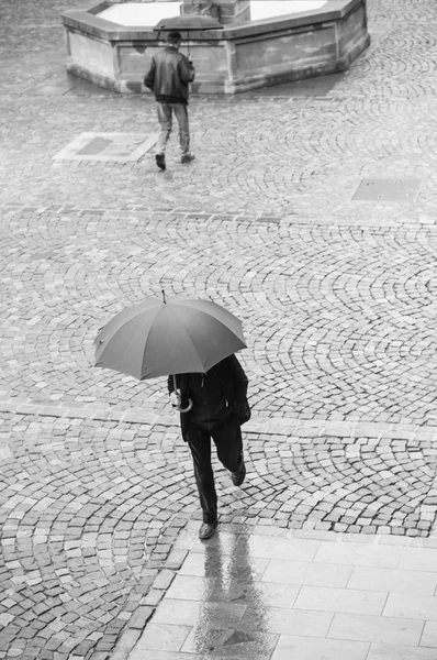 Portrait of men with umbrella on cobbles place with fountain in the city — Stock Photo, Image