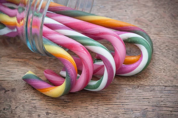 Candy canes on glass container on wooden background — Stock Photo, Image