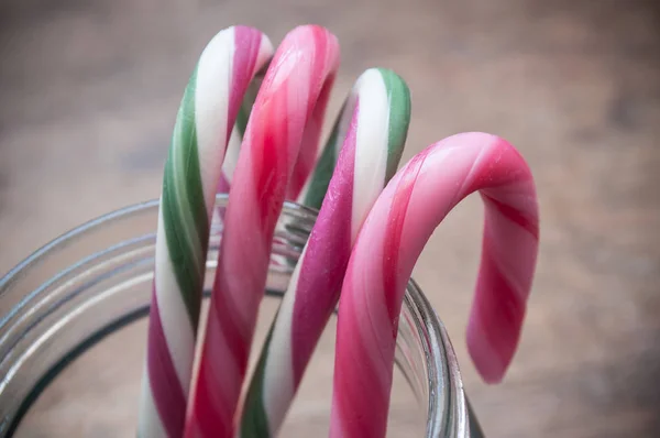 Candy canes on glass container on wooden background — Stock Photo, Image