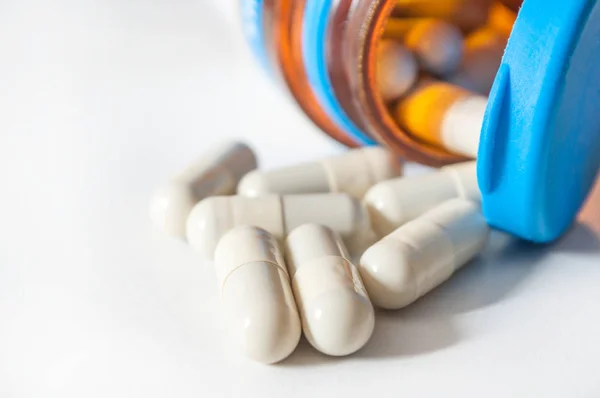 Cápsulas y tabletas de medicamentos que caen del frasco sobre fondo blanco Imágenes de stock libres de derechos