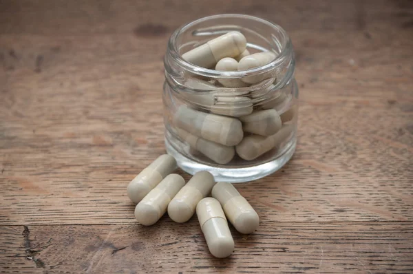 Capsules en tabletten van de drug en glazen fles op houten tafel — Stockfoto