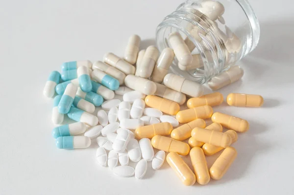 Капсули та таблетки, що падають з пляшки на білому тлі — стокове фото