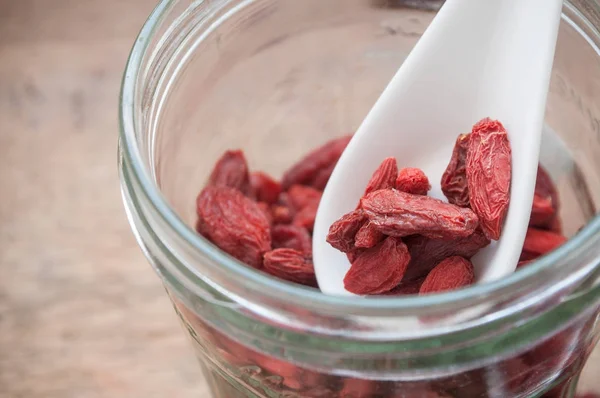 Goji bagas em colher chinesa e frasco de vidro em fundo de mesa de madeira — Fotografia de Stock