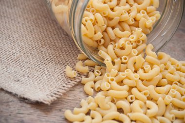  cam kapsayıcıdan ahşap masanın üzerine düşen makarna 