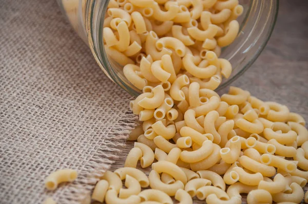 Pasta que cae del recipiente de vidrio en la mesa de madera — Foto de Stock