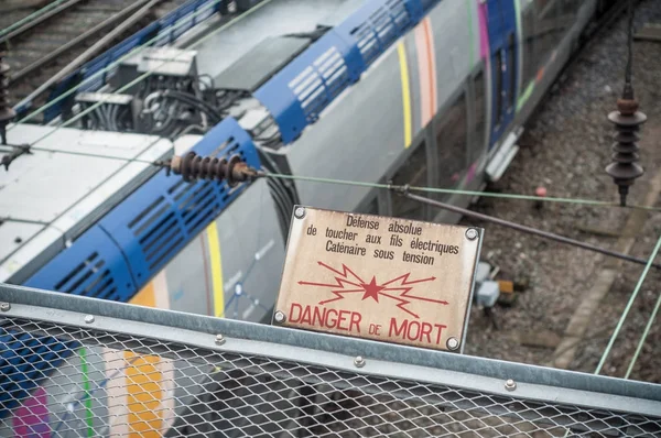 危险标志在路轨与火车通过下面 (文本在法语) — 图库照片