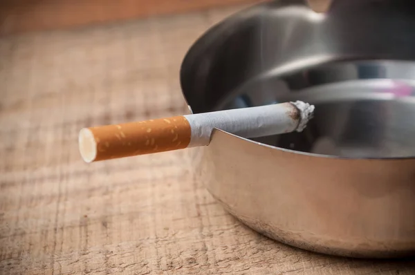 Cigarro no cinzeiro no fundo de madeira — Fotografia de Stock
