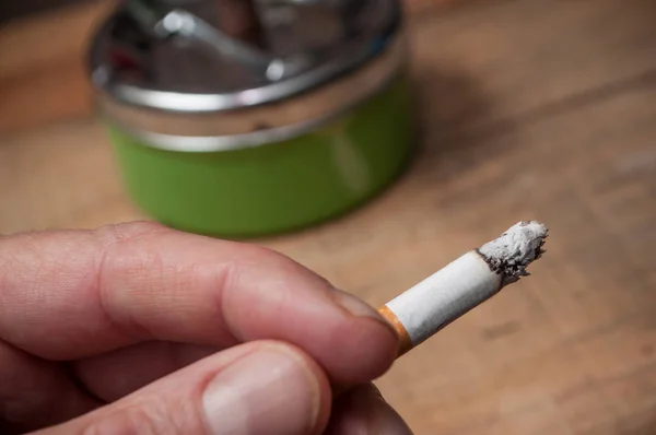 Cigarrillo en la mano sobre fondo cenicero borroso — Foto de Stock