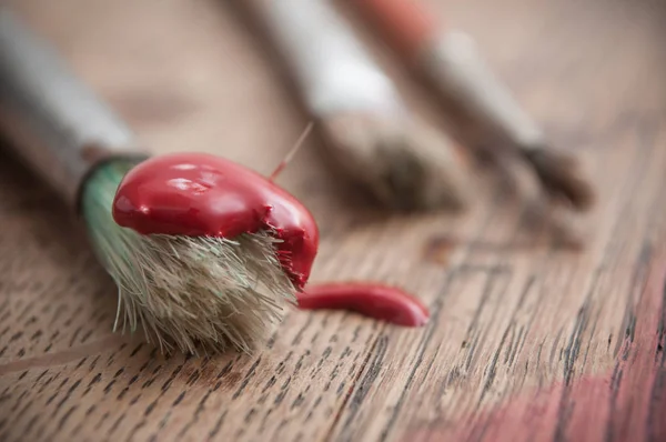 Tinta acrílica vermelha em pincéis em fundo de mesa de madeira — Fotografia de Stock