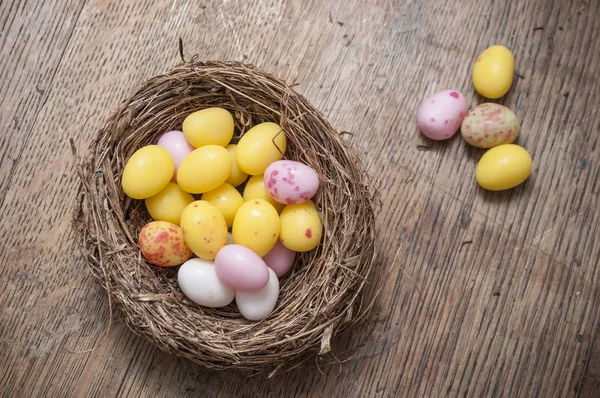 mini colorful easter eggs in nest on wooden background