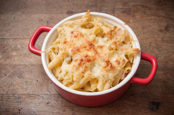 Gratin of pasta in a red porcelain dish on wooden table — Stock Photo, Image