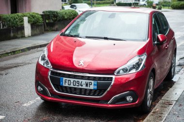 Yağmurlu bir günde caddeye park edilmiş kırmızı Peugeot 208 'in ön görüntüsü