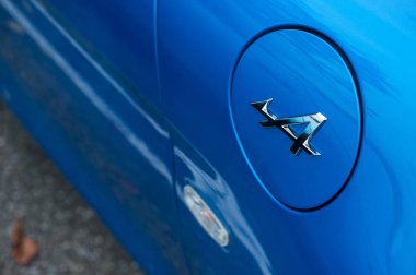  Alp logosu, caddeye park edilmiş mavi Alp arabasının tank kapısında.