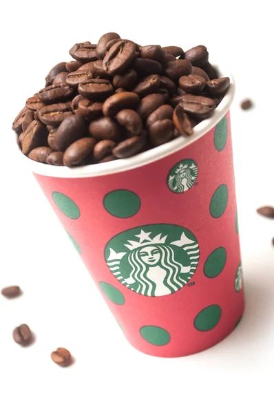 Кавові зерна в веселих кристалах забирають чашку з марки Starbucks на білому тлі. — стокове фото