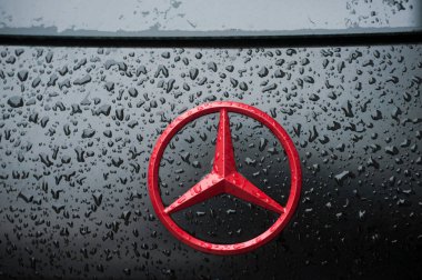 Sokakta park etmiş siyah Mercedes 'in üzerine kırmızı logo damlatıyor.