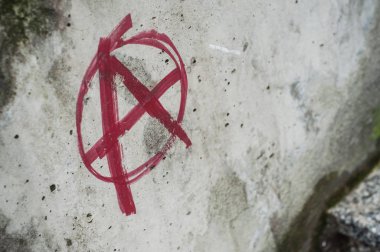 Closeup of red anarchy symbol painted on cement wall in the street clipart
