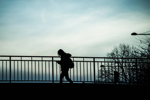 Silhouette eines Mädchens, das mit Smartphone auf Brücke unter dem Fluss geht — Stockfoto