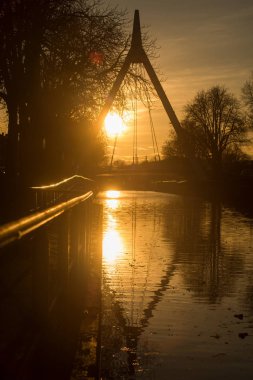Kanalın altında asılı köprü siluetiyle günbatımına kadar yansıması olan panorama