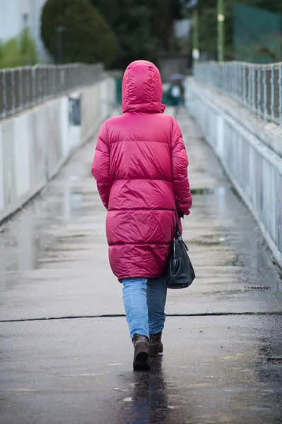 Mulher com capa de chuva rosa andando na rua — Fotografia de Stock