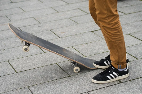 Jambes de patineur portant des baskets noires par Adidas attendant avec planche à roulettes dans la rue — Photo