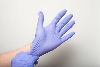 Beyaz arka plandaki koronavirüs salgınından korunmak için lateks eldiven takan bir kadının ellerine yakın çekim.