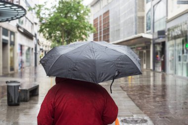 Sokakta kırmızı ceketli ve siyah şemsiyeli bir kadın portresi