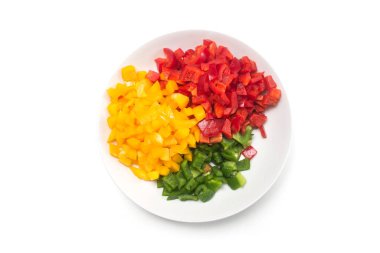 Beyaz arka planda beyaz bir tabakta kesilmiş organik biber parçalarının çeşitli renklerinin yakın plan görüntüsü