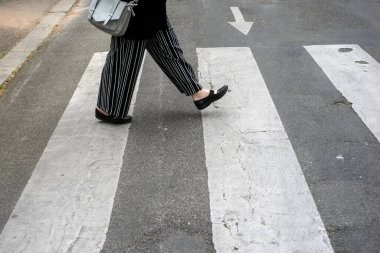 Kavşaktaki zebra üzerinde yürüyen çizgili pantolonlu bir kadının bacakları.