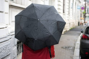Sokakta kırmızı ceketli ve siyah şemsiyeli bir kadın portresi