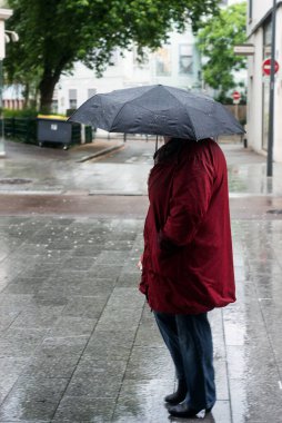 Sokakta kırmızı ceketli ve siyah şemsiyeli bir kadın portresi