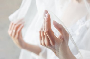 Güzel manikürlü gelinin elleri duvağı tutuyor. Evlilik kavramı, daha parlak bir gelecek ve romantizmin vücut bulmuş hali. Doğal düğün manikürü. Yakından bakımlı ve narin eller..