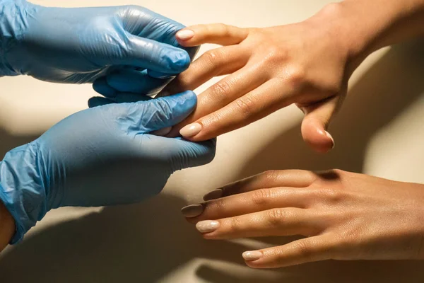 Manicure in handschoenen houdt handen van de klanten hand. — Stockfoto