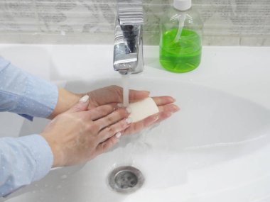 İnsanlar bir kalıp sabunla lavaboda ellerini yıkıyor. Alkol bazlı el dezenfektanı ve antibakteriyel sabunla Coronavirus hastalığını öldürüyorlar. Akan sulardaki mikroplarla savaşmak için. Evde kal ve ellerini yıka.