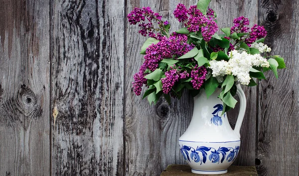 vase with a bouquet of multi-colored lilacs. White vase with a blue pattern. Background old wood. Retro style Concept. Copy space.