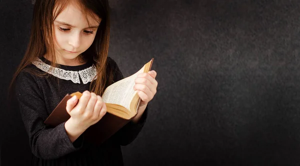 Beyaz dantel yakalı gri yün elbiseli küçük kız kahverengi kapaklı bir kitap okuyor. Retro tarzı. Arka plan gri. Evde eğitim kavramı. Kitap okuma aşkı. Boşluğu kopyala