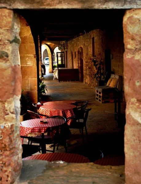 Verandada güneş ışınlarıyla aydınlatılmış kırmızı halıları olan masalar. Taş bir çerçeve tarafından çerçevelenmiş.