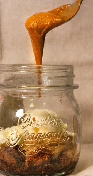 Peanut butter falling from a spoon to flavor a dessert that is in a glass jar.