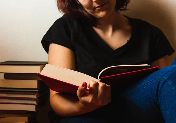Yanında bir sütun kitapla yerde oturmuş kitap okuyan bir kadın..