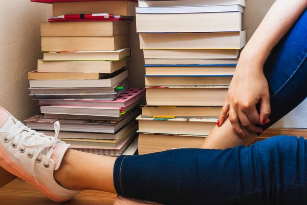 Evdeki oturma odasında güneşli bir günde arka planda kitap sütunları olan kız bacakları yere uzanıyordu..