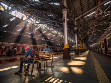 Mumbai, Hindistan - 18 Aralık 2019: Mumbai 'deki işçi sınıfının en yoğun tren istasyonlarından biri olan CST istasyonunda sabahın erken saatlerinde güneşli bir bankta oturan kimliği belirsiz yolcular