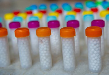 Beyaz homeopatik haplarla dolu renkli plastik şişeler.