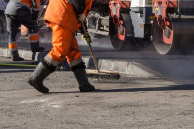 Eski asfaltın yenilenmesi sırasında, turuncu üniformalı yol işçileri kaldırım operasyonu için yüzeyleri hazırlıyorlar.