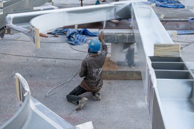 Ressam çelik yapıdaki boyayı endüstriyel fabrikada sprey tabancayla ateşe dayanıklı hale getirmeye çalışıyor..